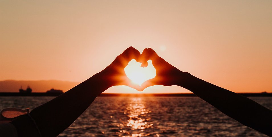 Två personer i en solnedgång som format ett hjärta med sina händer.