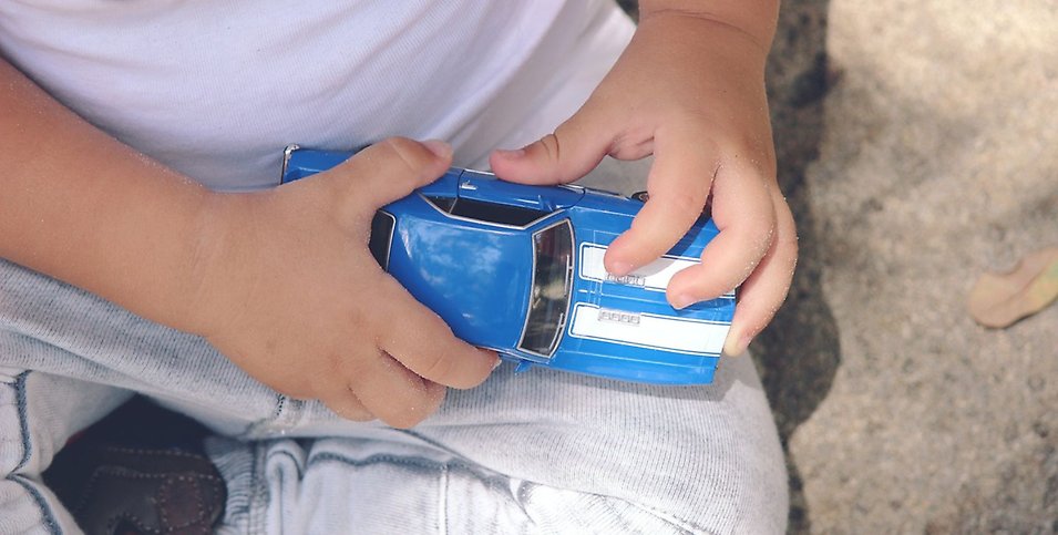 Ett barn sitter i en sandlåda och leker med en blå bil.