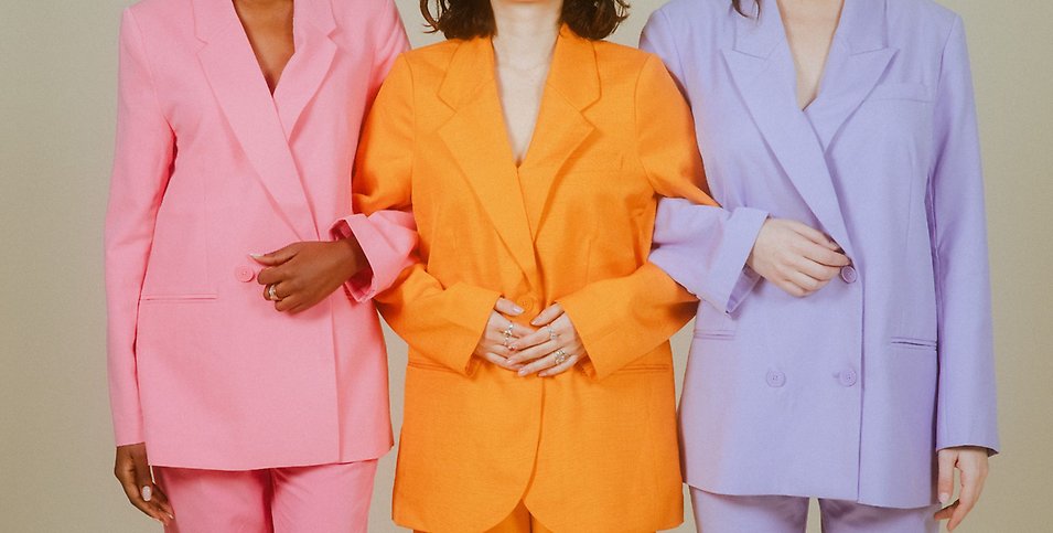 Tre kvinnor i färgglada kostymer krokar arm.