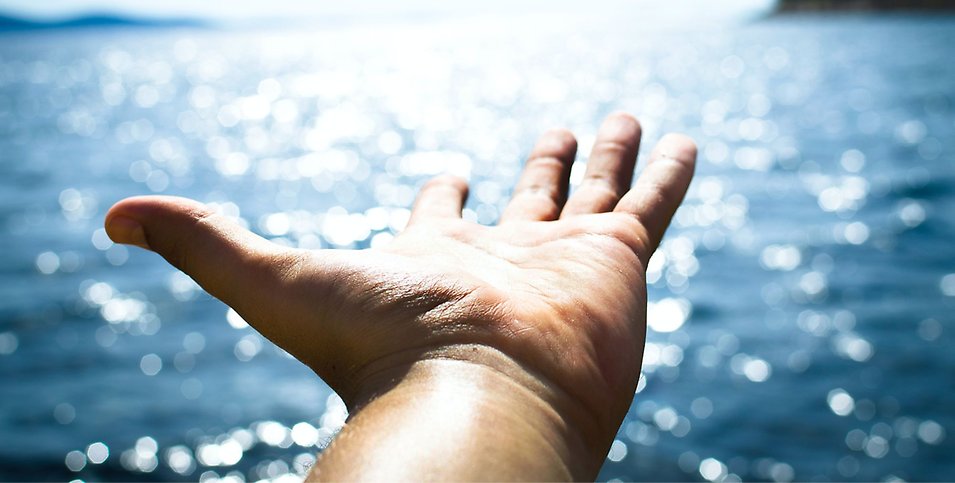 En utsträckt hand en solig dag vid havet.