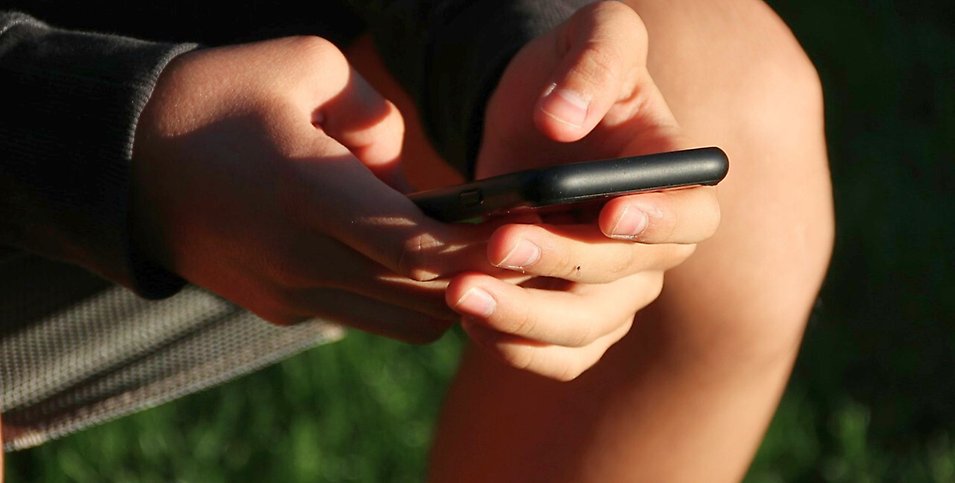 Ung person sitter med sin mobiltelefon en vår/sommar-dag.