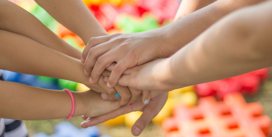 Flera barn håller händerna över varandra med leksaker i bakgrunden.