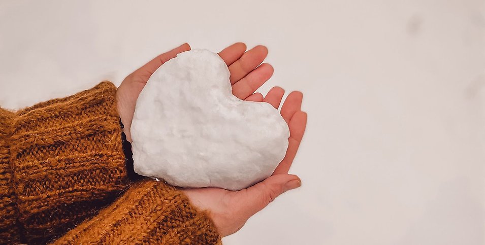 En person håller i ett hjärta av snö i sina händer.